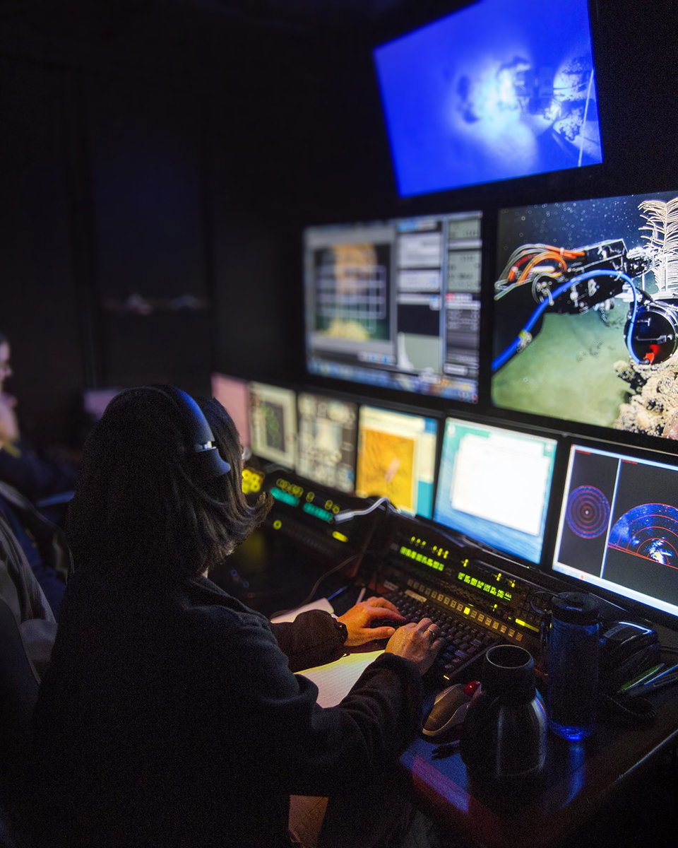Tecnico ROV donna al lavoro, pilotando il ROV e monitorando gli schermi nella control room per operazioni subacquee.